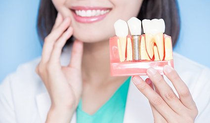 Smiling dentist holding model of dental implants in Park City