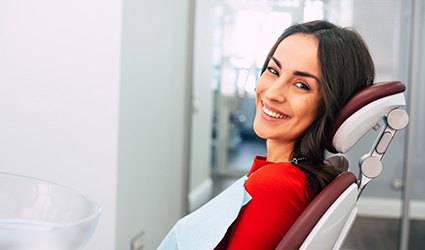 A young woman wearing a red blouse and smiling while in the dentist’s chair 