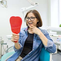 Woman at dentist’s office smiling into hand mirror