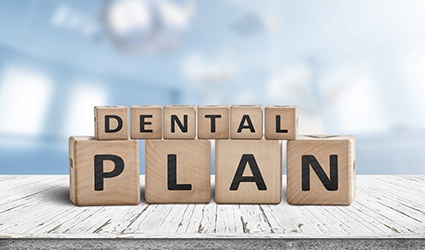 A set of blocks sitting on a white table and spelling the words “Dental Plan”