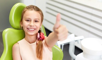 A young girl giving a thumbs up and smiling while in the dentist’s chair