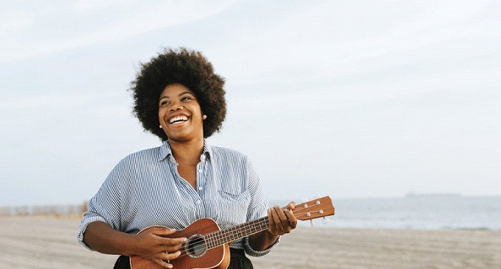 person playing a ukulele on a beach and smiling